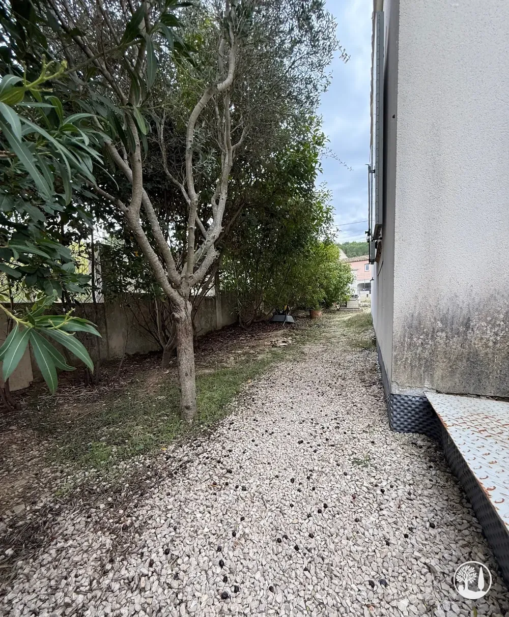 Avant : allée de gravier sous un arbre, le long de la maison