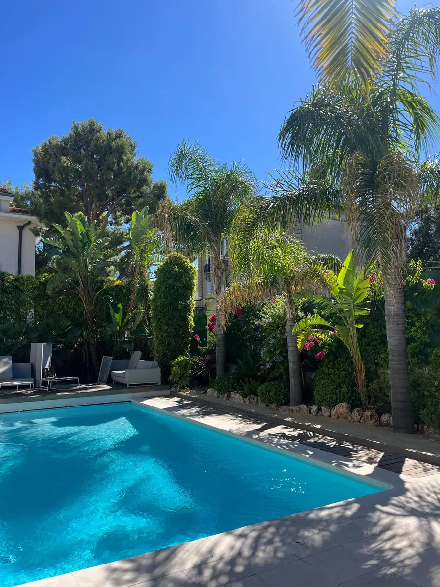 Jardin méditerranéen au bord d'une piscine : palmiers, bananiers et bougainvilliers en fleurs sous un ciel bleu